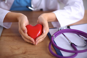 This is a picture of a doctor holding a heart with a purple stethoscope on her right with a clipboard under the stethoscope