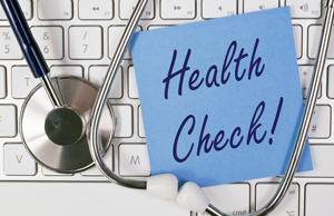 this a picture with a keyboard as the background with a stethoscope with a blue sticky note saying health check!
